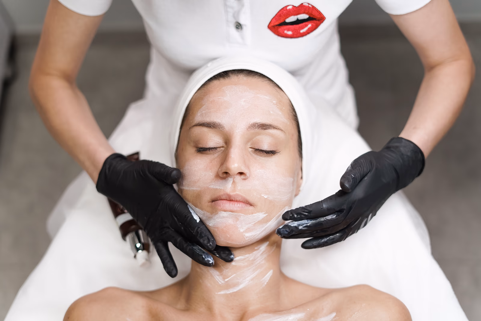 A beautician removing a clay mask from a client's face