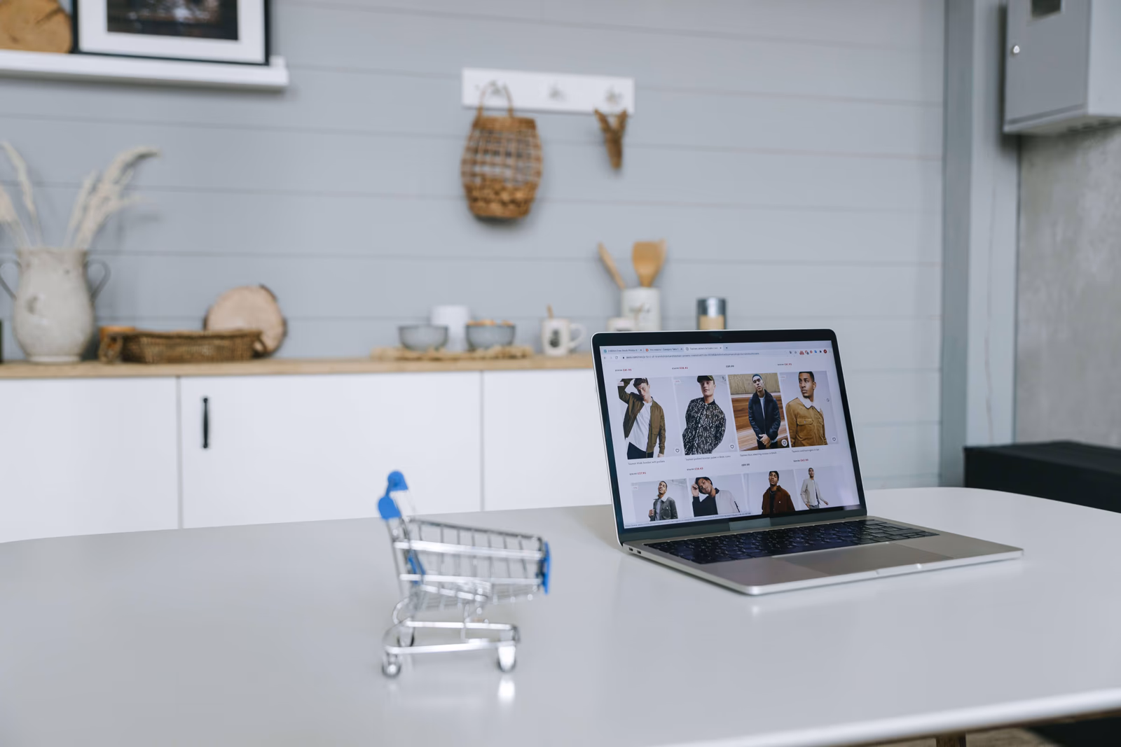 A laptop beside a miniature shopping cart