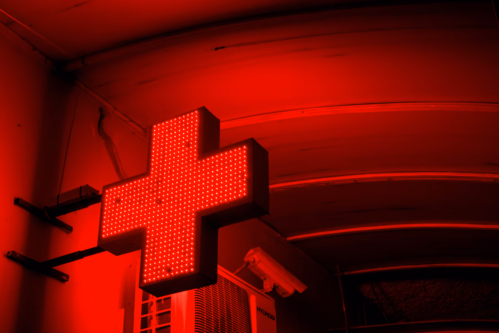 A glowing pharmacy cross sign at night