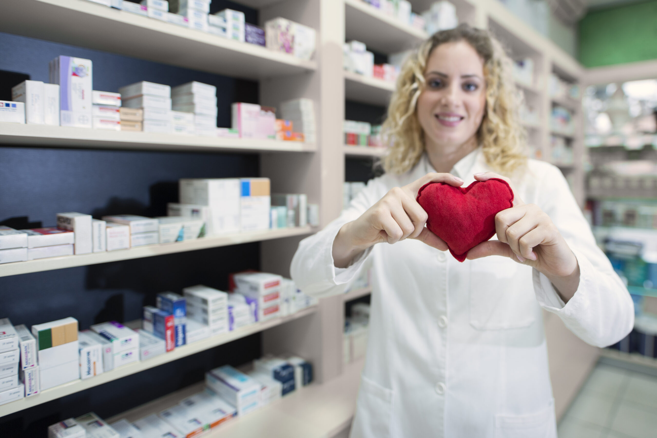 Female pharmacist holding heart and promoting cardiovascular medications and successful treatment. Wellness products